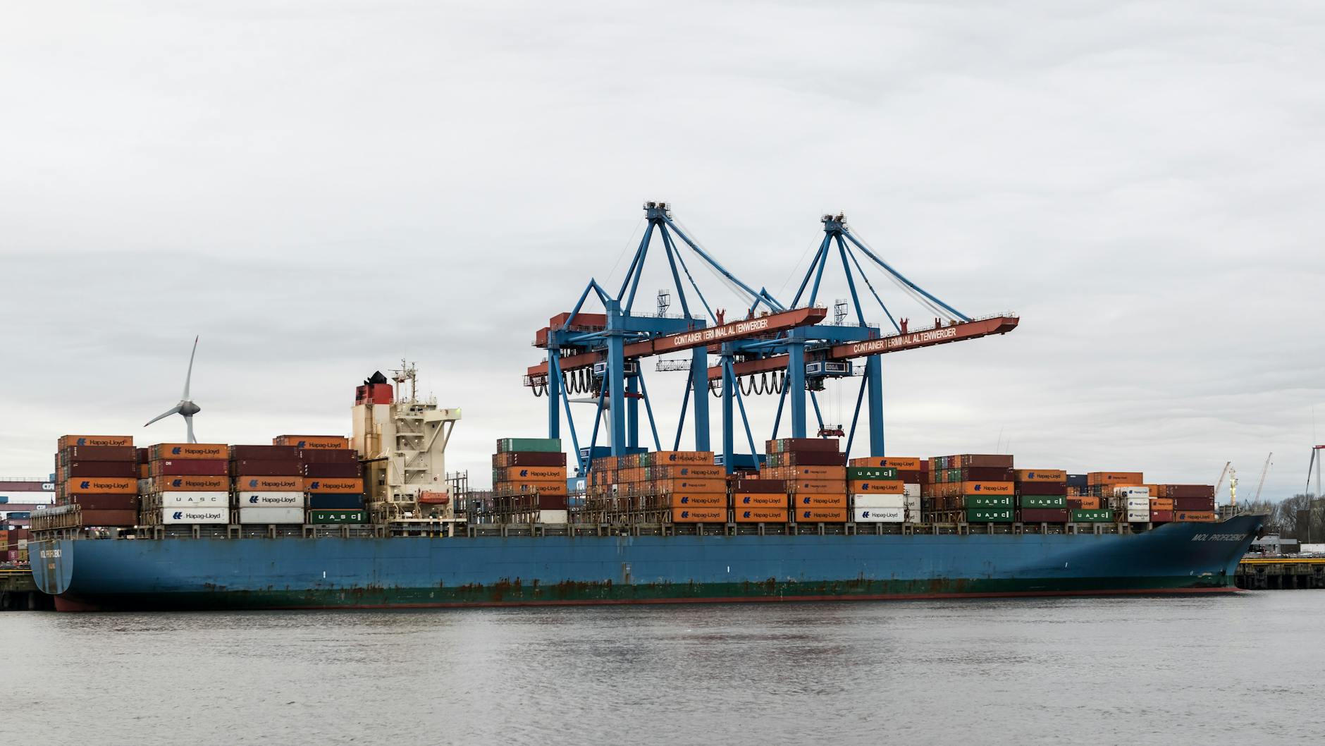 Large container cargo ship docked at industrial port with shipping containers