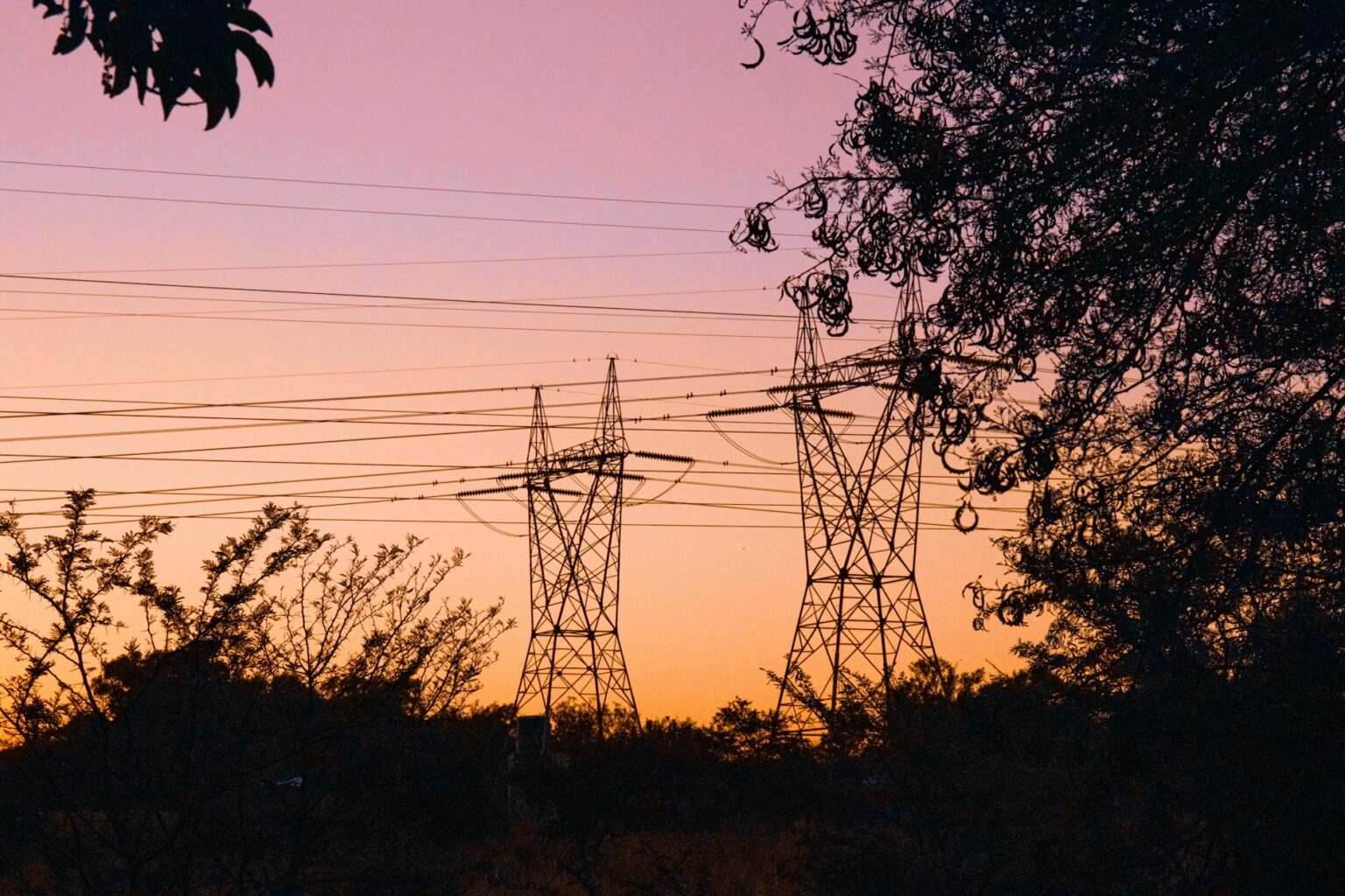 Electrical transmission lines silhouetted against sunset sky