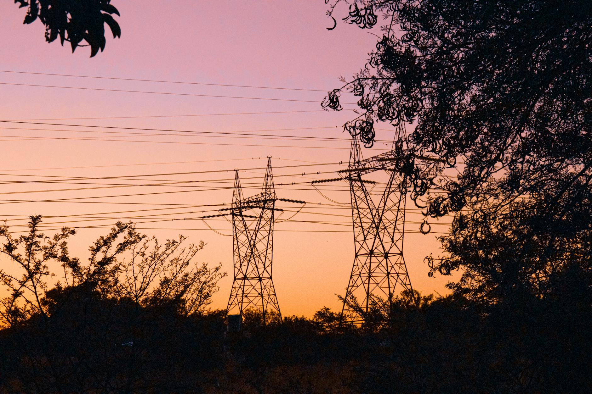 Electrical transmission lines silhouetted against sunset sky