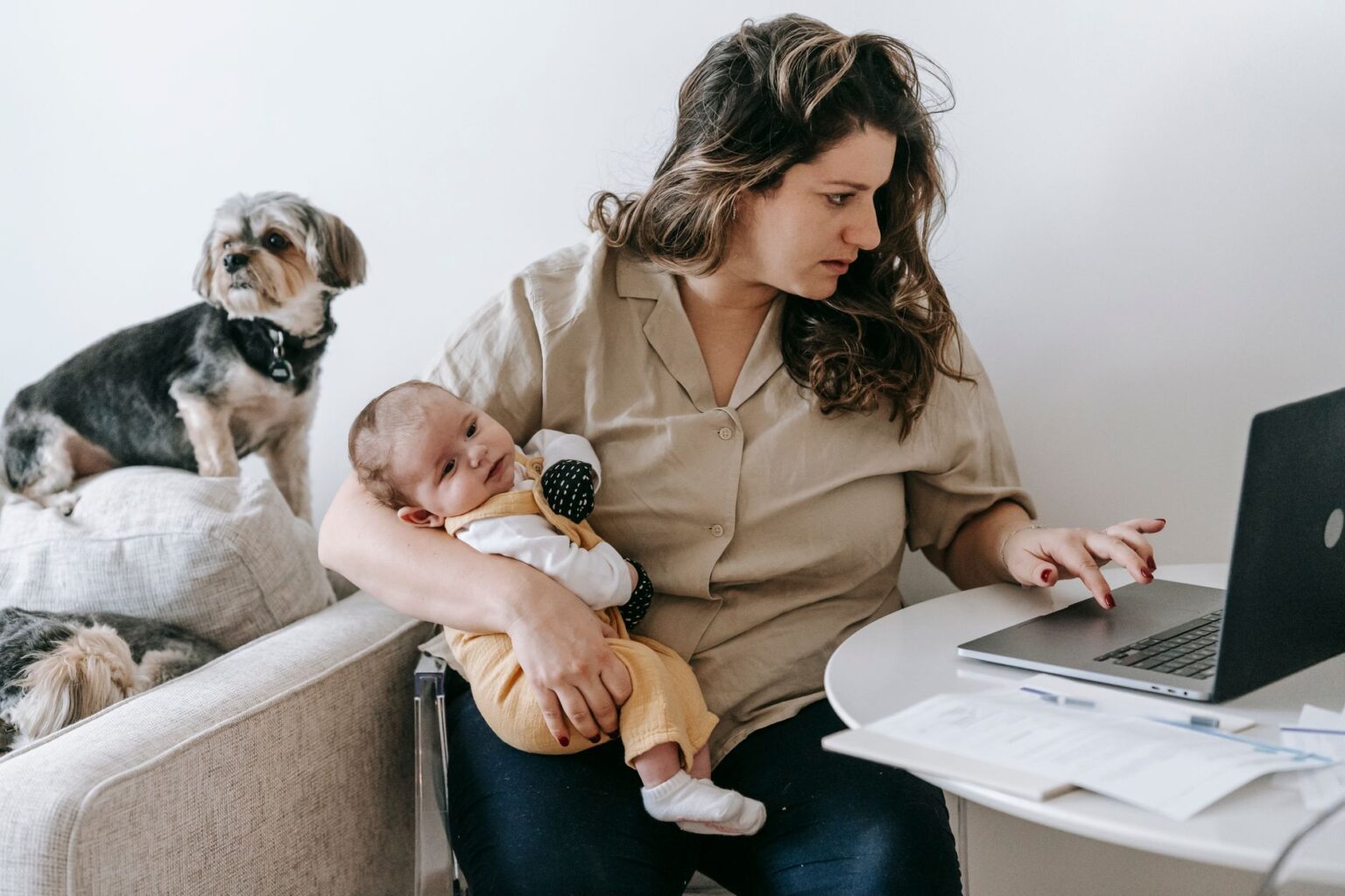 A working mother sits at a desk with paperwork, representing the financial pressures facing working parents navigating child care costs
