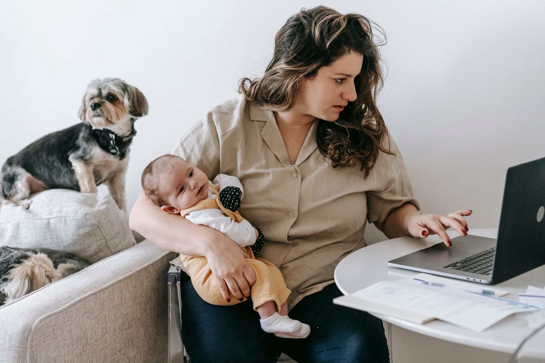 A working mother sits at a desk with paperwork, representing the financial pressures facing working parents navigating child care costs