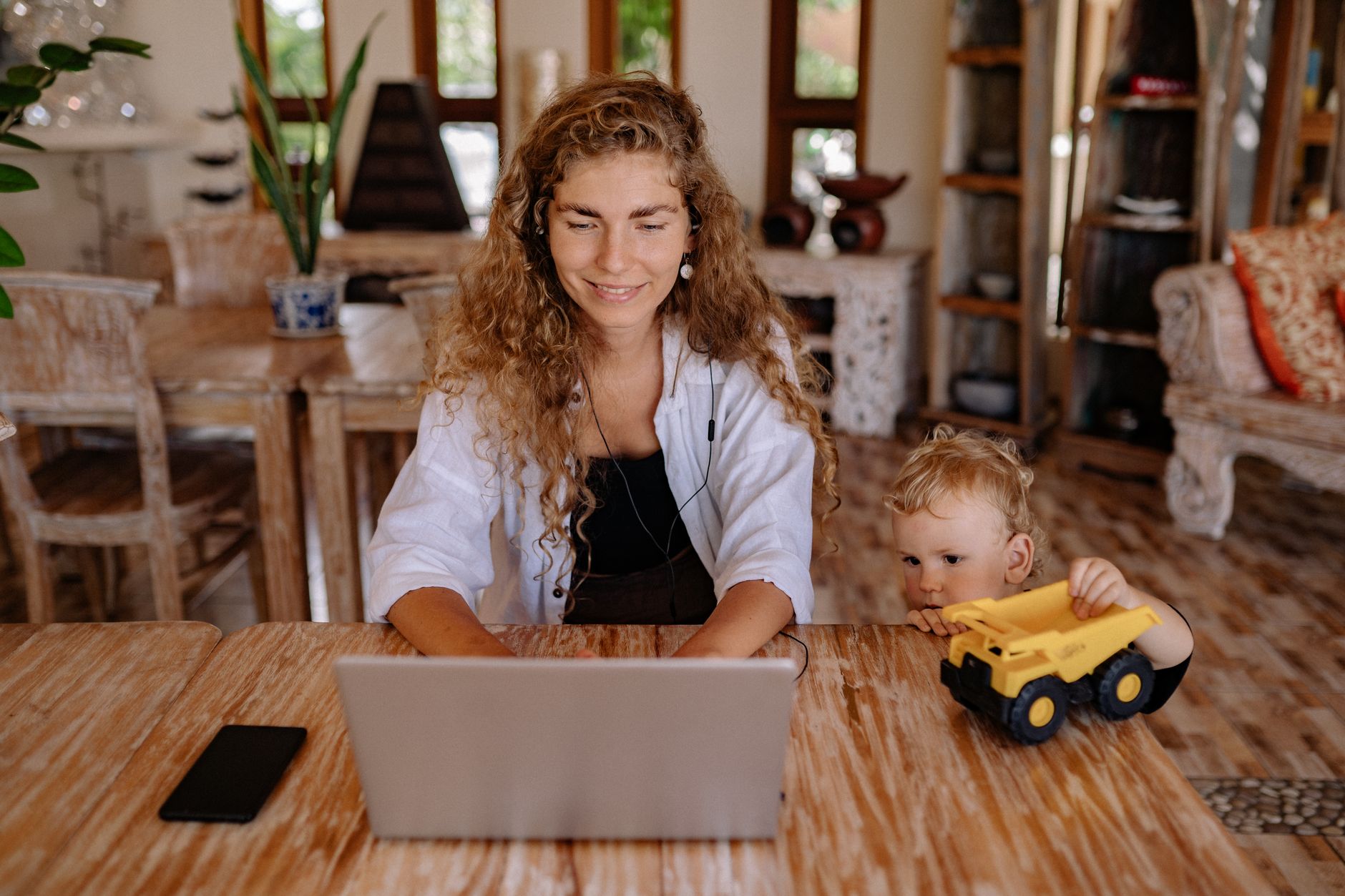 Mother working at a desk with a young child nearby, illustrating childcare and workforce pressures
