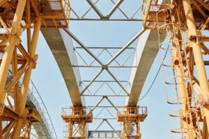 Large infrastructure construction site with cranes and steel framework against a clear sky