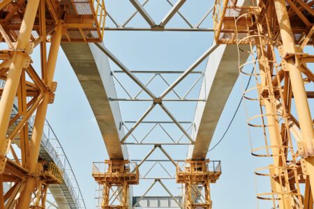 Large infrastructure construction site with cranes and steel framework against a clear sky