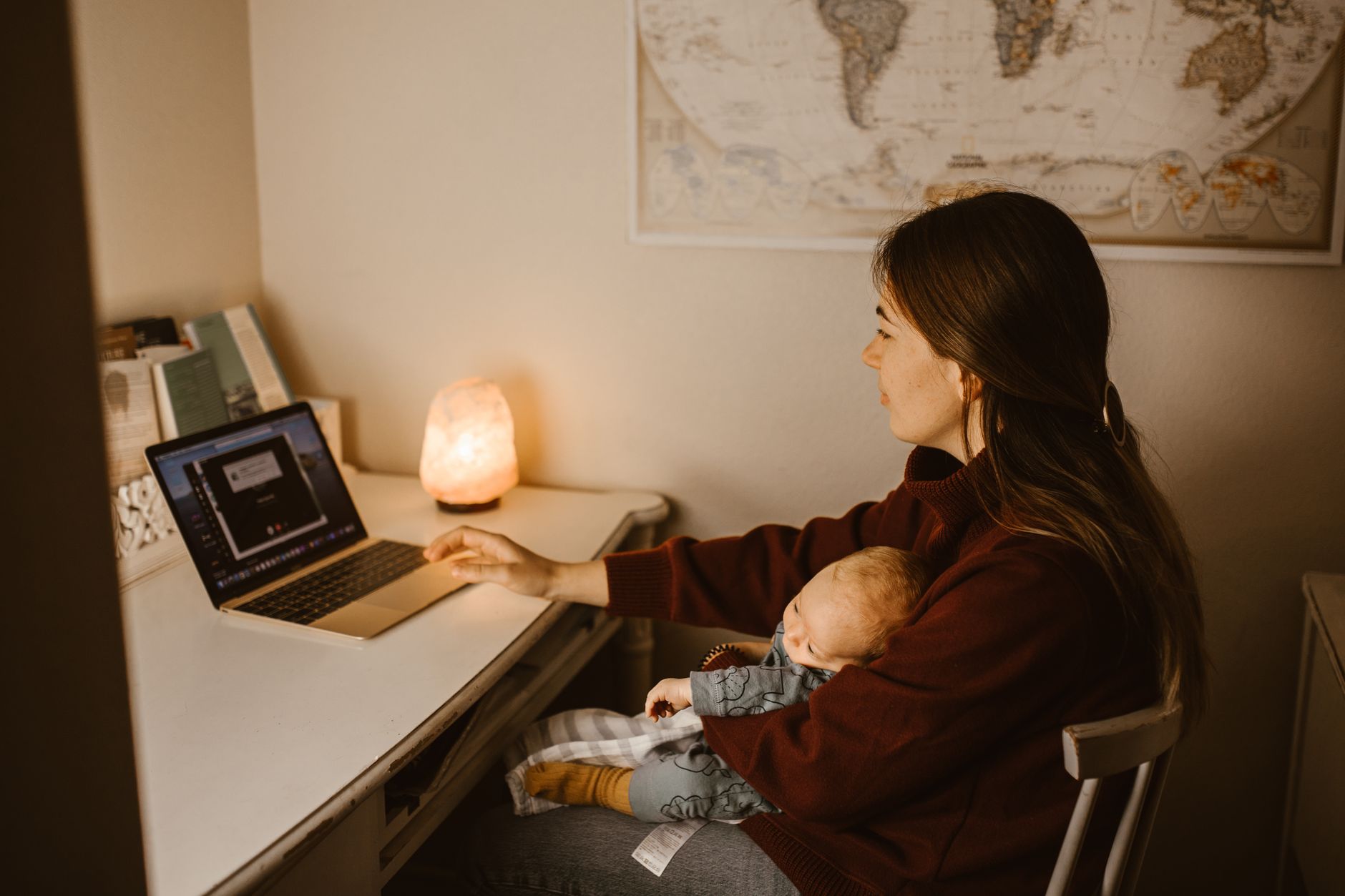 Working mother at a desk managing work responsibilities while caring for a child