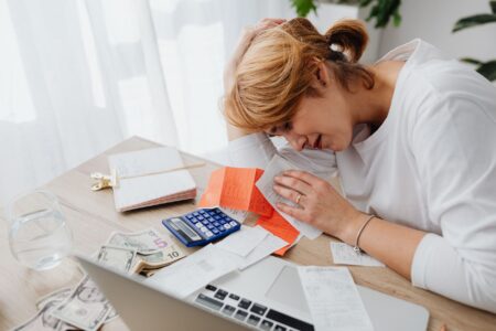 Student Loan Delinquencies Surge as Repayment Pause Protections Expire A person sitting at a desk looking stressed while reviewing financial documents and bills