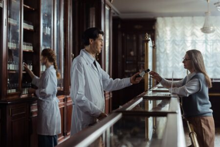 Pharmacy Benefit Manager Reform Stalls as Drug Cost Burden Shifts Pharmacist standing behind a pharmacy counter reviewing prescription medications