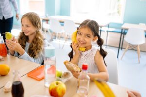Child Nutrition Waivers Expire as School District Meal Debt Mounts Students moving through a school cafeteria lunch line with trays of food